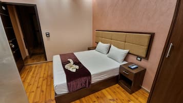 A neatly arranged bedroom with a wooden floor, a bed with white linens, a brown headboard, and a bedside table with a book.