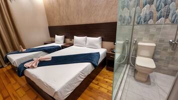 A hotel room with two beds, wooden flooring, a shower with a glass door, and a toilet.