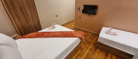 Habitación de hotel con dos camas, piso de madera, televisor montado en la pared y puerta de madera.