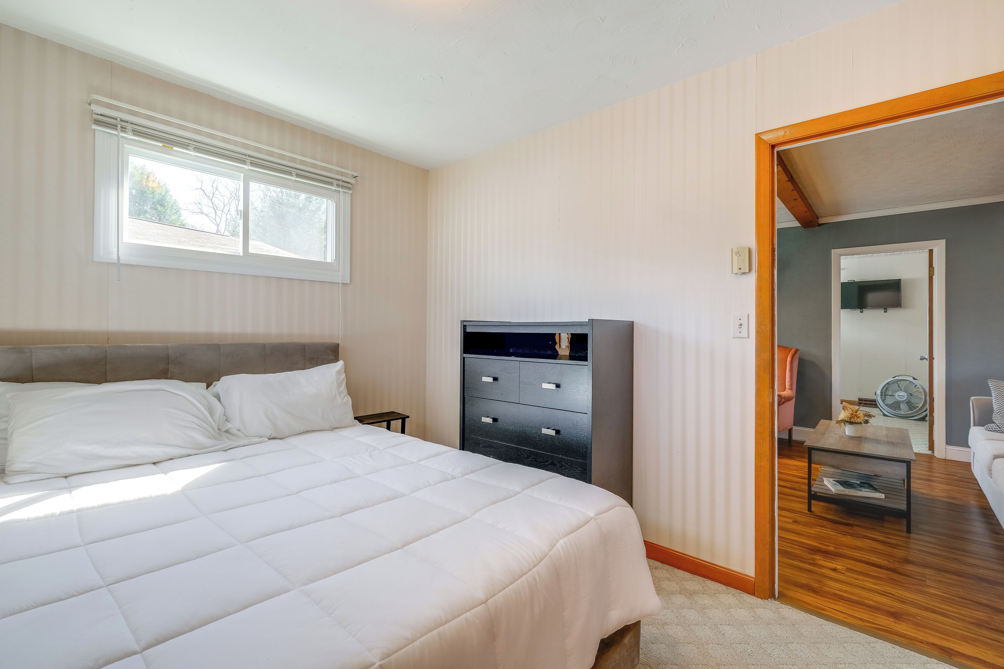 Quarto com cama, penteadeira, janela e porta que dá para outro espaço.
