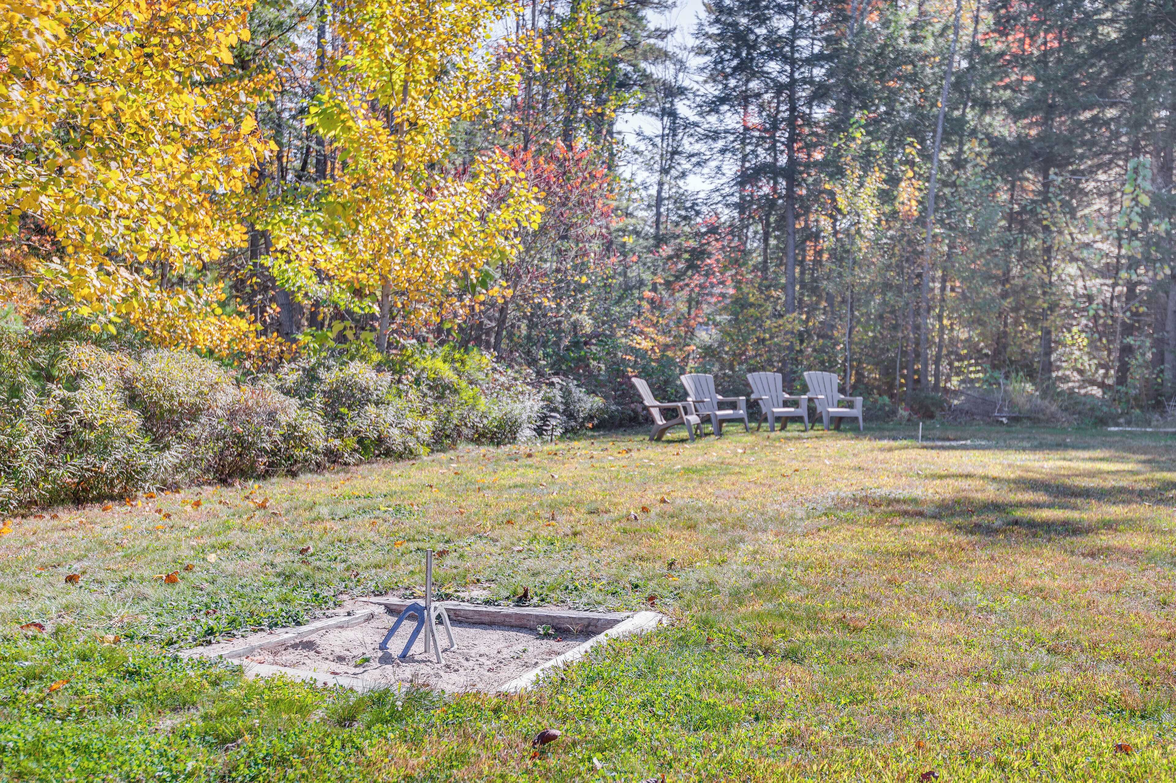 Un espacio cubierto de césped con una hoguera y sillones Adirondack en un entorno boscoso.