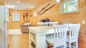 Interno di una baita in legno con un tavolo da pranzo, sedie, un divano e una finestra vista alberi.