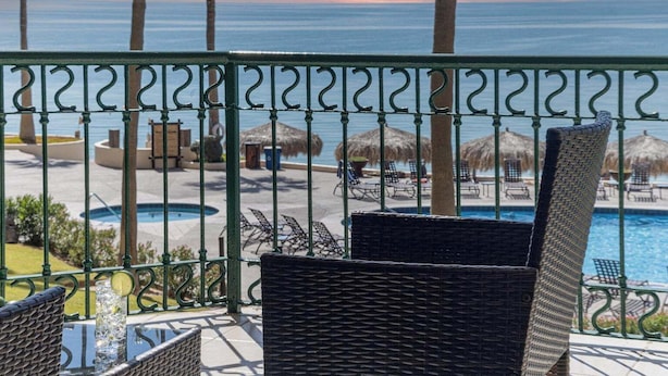 Ein Balkon mit Korbmöbeln, einem Pool und Blick aufs Meer.