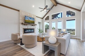A spacious living room with a stone fireplace, a large TV, and a comfortable seating area with a view of the outdoors.