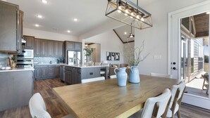 Una cocina moderna con una isla central, mesa de comedor de madera y una lámpara colgante.