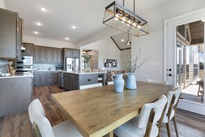 A modern kitchen with a central island, wooden dining table, and a hanging light fixture.