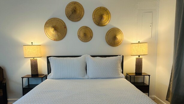 A bed with a white quilted bedspread, two white pillows, and a headboard. There are four wall-mounted lamps with a woven design. - Wilton Manors Guesthouse #6 (Wilton Manors)