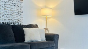 A modern living room with a grey sofa, white cushions, a wooden coffee table, and a wall-mounted lamp. - Wilton Manors Guesthouse #6 (Wilton Manors)