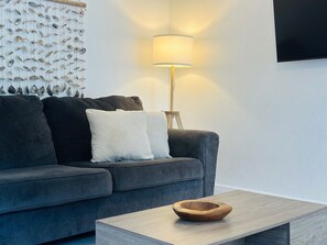 Ein modernes Wohnzimmer mit grauem Sofa, weißen Kissen, einem Holztisch und einer Wandlampe.