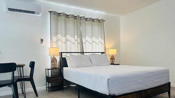 Une chambre à coucher avec un lit, deux tables de chevet avec des lampes, une chaise et une fenêtre avec des rideaux.