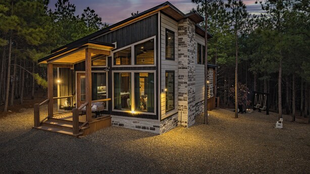 A modern two-story cabin with a stone facade, large windows, and a wooden deck. - Couples Retreat: Sauna, Massage Chairs, Hot Tub (Broken Bow)