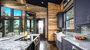A modern kitchen with a large island, dark cabinetry, and a view of the outdoors. - Couples Retreat: Sauna, Massage Chairs, Hot Tub (Broken Bow)
