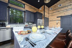 A modern kitchen with dark cabinets, a granite countertop, and a breakfast setup with plates, glasses, and a fruit bowl. - Couples Retreat: Sauna, Massage Chairs, Hot Tub (Broken Bow)