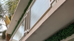 A building with a glass facade, a white car parked in front, and greenery on the upper level. - Hotel Galería & Boutique (Mexico City)