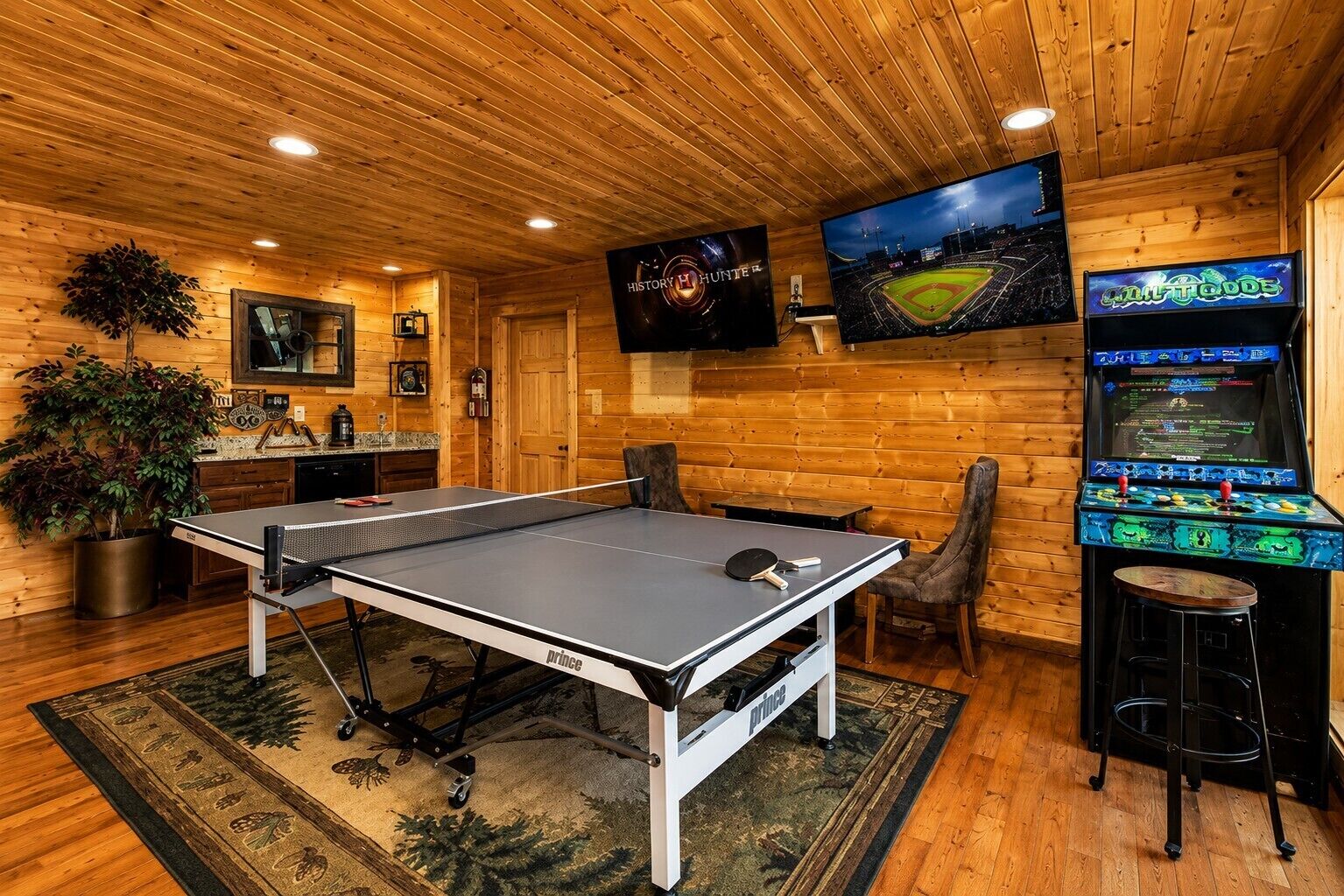 A room with a ping pong table, a bar area, and a video game machine.