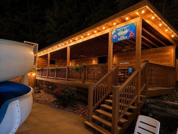 A wooden covered pavilion with a pool, stairs, and a sign advertising a call to reserve.