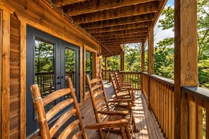 A wooden deck with chairs and a glass door, overlooking a forested area. - Luxury Cabin w/ All-Inclusive Resort Amenities (Pigeon Forge)