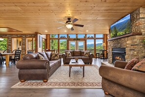 A spacious living room with leather sofas, a fireplace, and a large window overlooking a mountainous landscape.