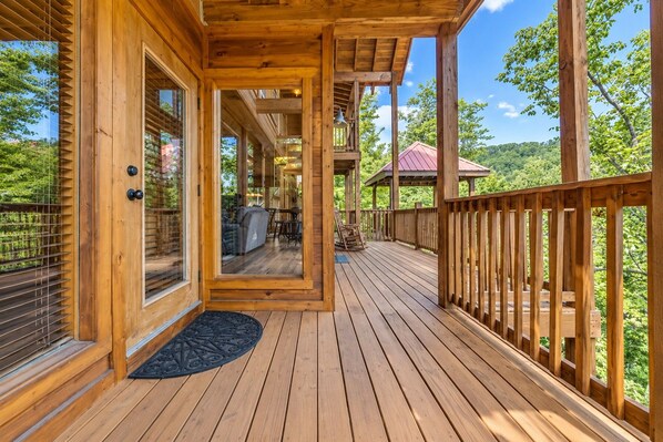A wooden deck with a covered area, a view of the outdoors, and a door leading to an interior space.