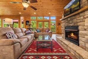 A cozy living room with a stone fireplace, leather sofas, and a red patterned rug.