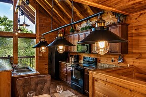 A wooden interior with a kitchen area featuring a refrigerator, oven, and microwave. There are pendant lights hanging above the counter.