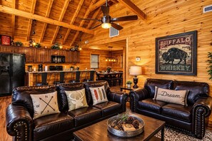 A cozy cabin interior with a leather sofa set, a dining area, and a kitchen. - Cabin + FREE Resort Amenities | Pigeon Forge (Pigeon Forge)
