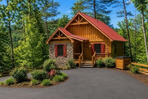 A log cabin with a stone foundation, a red roof, and a wooden porch. - Cabin + FREE Resort Amenities | Pigeon Forge (Pigeon Forge)