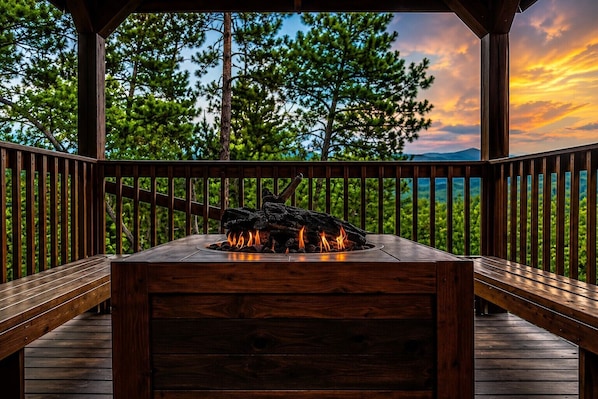 A wooden deck with a built-in fire feature, surrounded by trees and a scenic view.