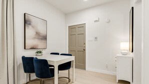 A dining area with a white table, blue chairs, and a painting on the wall. - Orchid: Studio Apt, 4 Minute Walk to A&M (College Station)