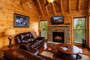 A cozy cabin interior with a leather sofa, a fireplace, and a television.
