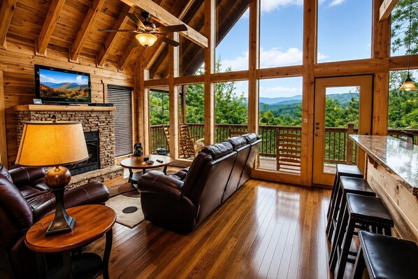 A cozy interior with a fireplace, leather seating, and a large window overlooking a scenic landscape.