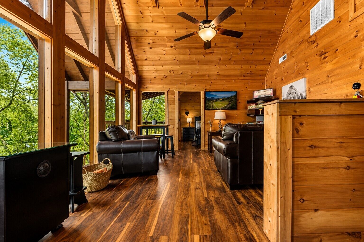 A spacious wooden cabin interior with a ceiling fan, large windows, a fireplace, and a dining area.