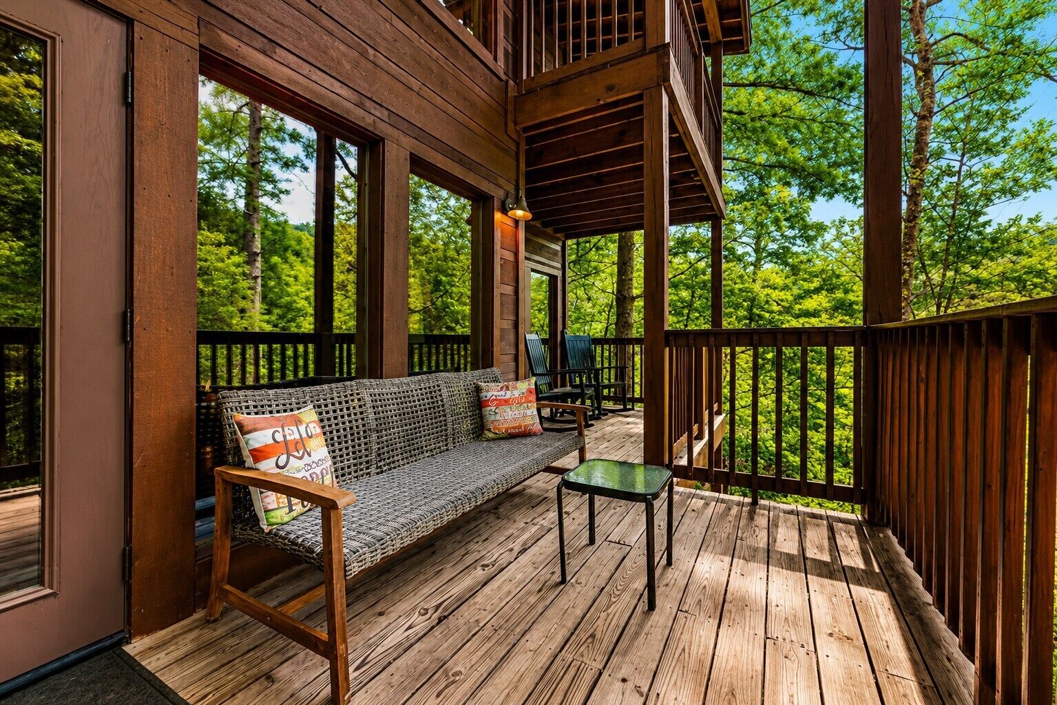 Une terrasse en bois avec un canapé et des fauteuils, une petite table et une rambarde donnant sur une forêt.