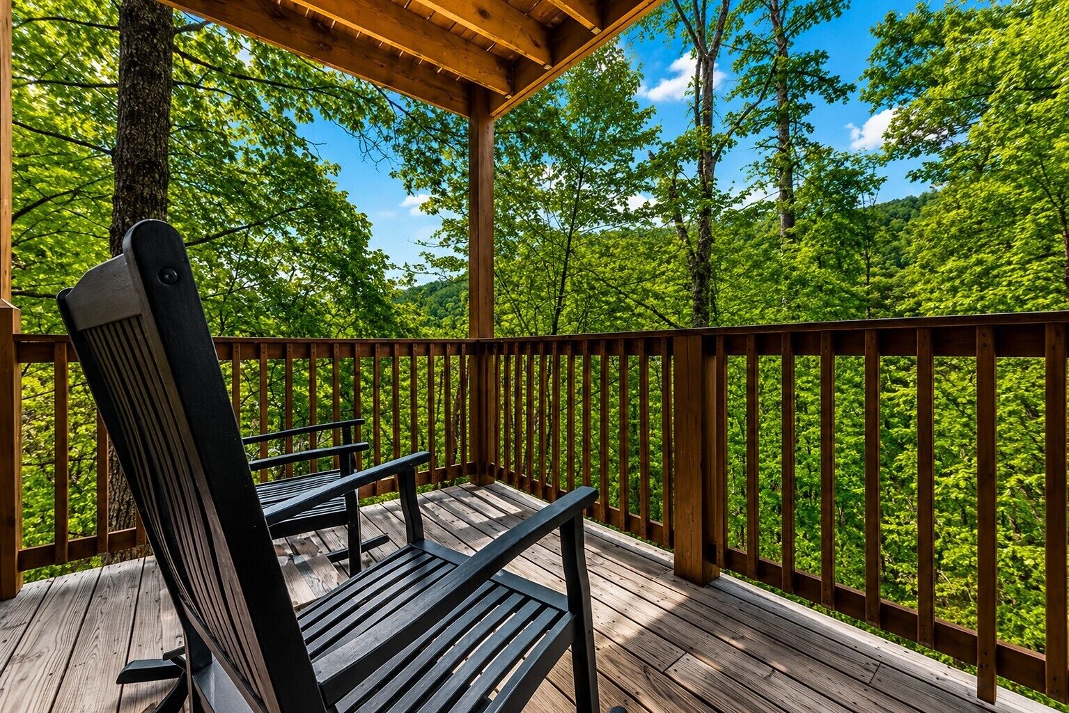 A wooden deck with a bench and table, surrounded by a wooden railing, overlooking a forested area.