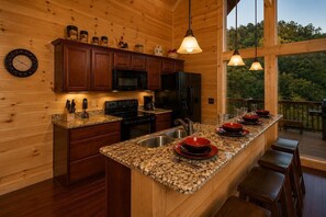 A kitchen with wooden walls, granite countertops, a central island with red bowls, and a view of the outdoors.