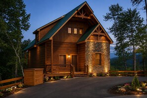 A log cabin with a stone foundation, a porch, and a mountain backdrop. - Cabin + FREE Resort Amenities | Pigeon Forge (Pigeon Forge)