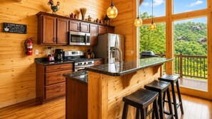 Cocina rústica con paredes de madera, una isla central con taburetes, microondas, estufa, refrigerador y extintor.