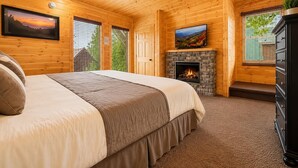 Un dormitorio de cabaña de madera con cama, chimenea, televisor y ventilador de techo.