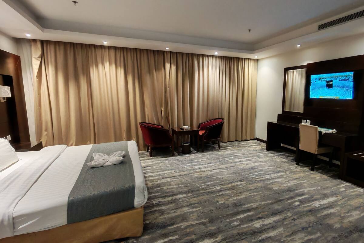 Une chambre d’hôtel comprenant un lit, un bureau avec une chaise, une télévision et une grande fenêtre avec des rideaux.