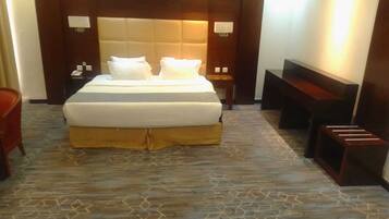 Una habitación de hotel con una cama grande, cabecera de madera, mesita de noche, un banco y suelo estampado.
