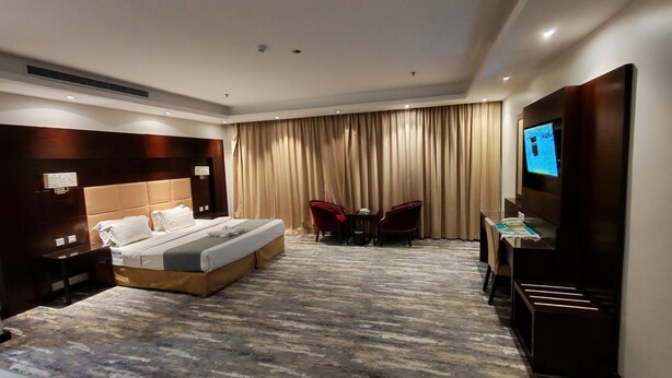 A hotel room with a large bed, a TV, a desk with two chairs, and a curtain backdrop. - Arjan Almutamyezah serviced apartments (Jeddah)
