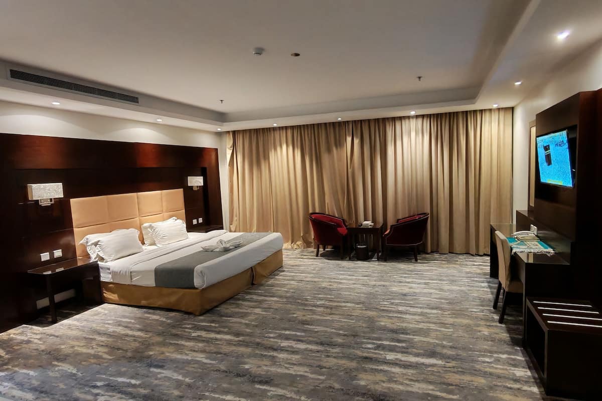 Une chambre d’hôtel avec un grand lit, une télévision, un bureau avec deux chaises et un rideau en arrière-plan.