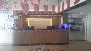 A reception desk with a wooden finish and a marble base, flanked by red and white patterned banners. - Arjan Almutamyezah serviced apartments (Jeddah)
