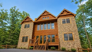 A two-story log cabin with a stone facade, large windows, and a wooden front porch.