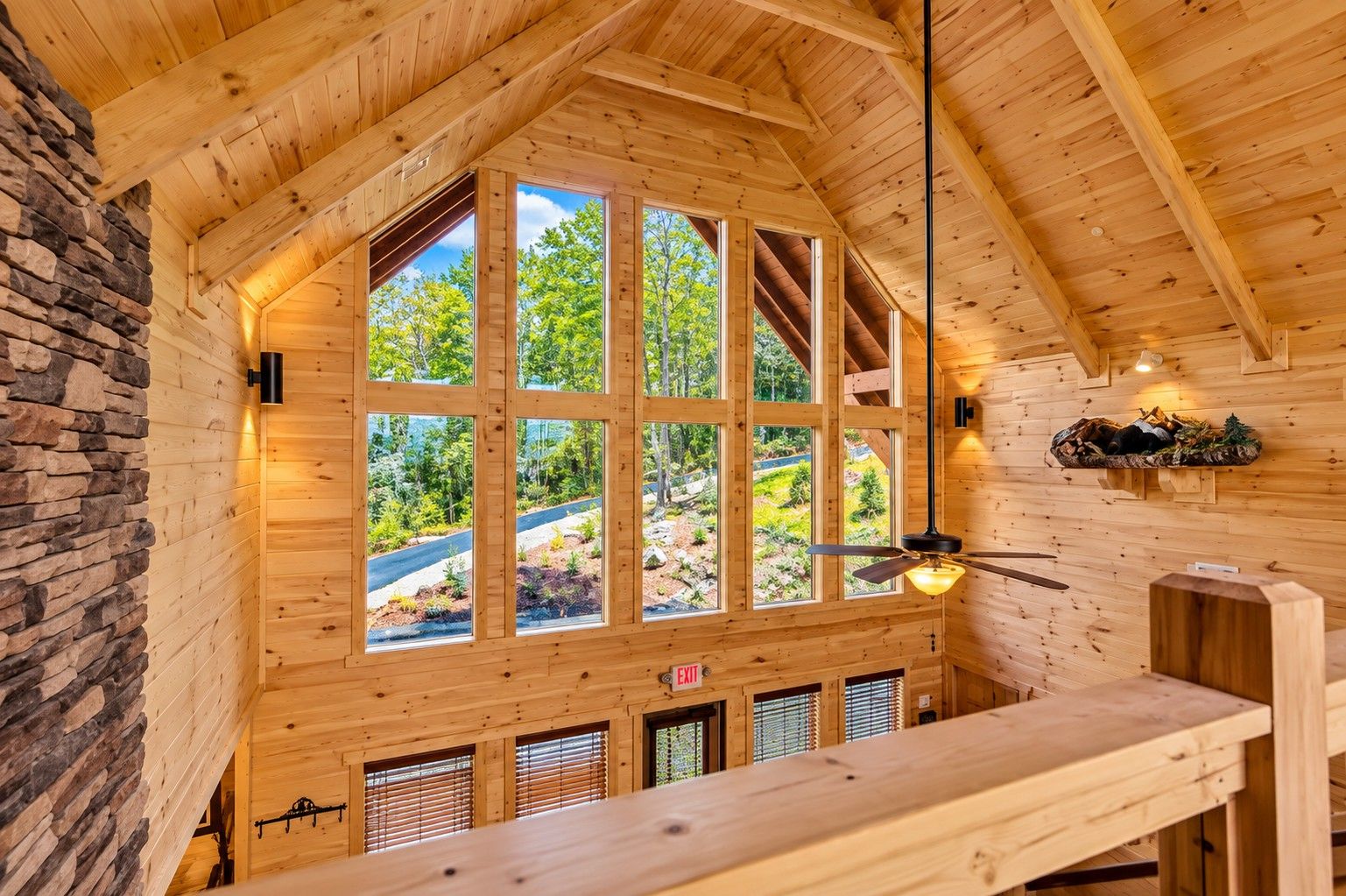 A wooden interior with large windows, a ceiling fan, and a stone wall.