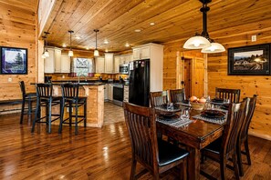 A wooden interior with a dining table set for four, kitchen cabinets, and a refrigerator.