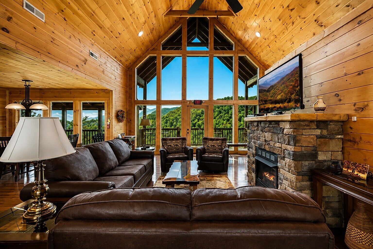 A spacious living room with a large fireplace, leather sofas, and a view of the outdoors.