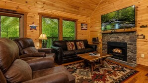 A cabin interior with a stone fireplace, leather furniture, and a television mounted above it. - Cabin + FREE Resort Amenities | Pigeon Forge (Pigeon Forge)