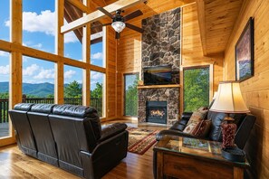 A spacious living room with a stone fireplace, leather sofas, and a large TV. - Luxury Cabin w/ All-Inclusive Resort Amenities (Pigeon Forge)