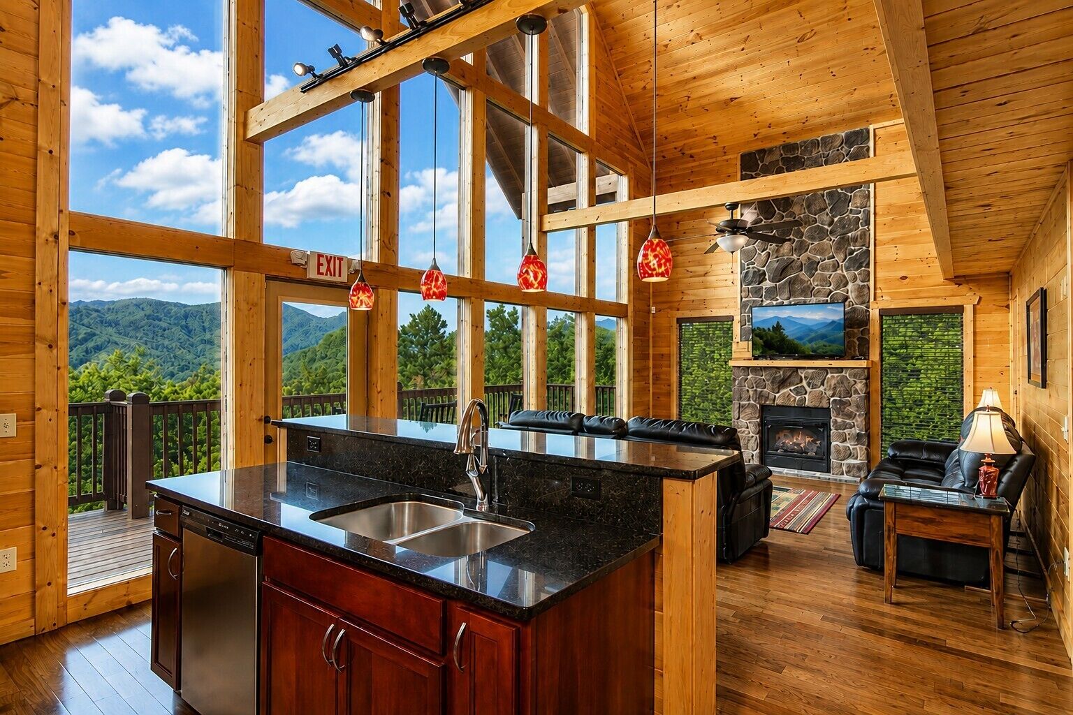 Interior de una cabaña con isla de cocina, comedor, chimenea y terraza con vistas a montañas.